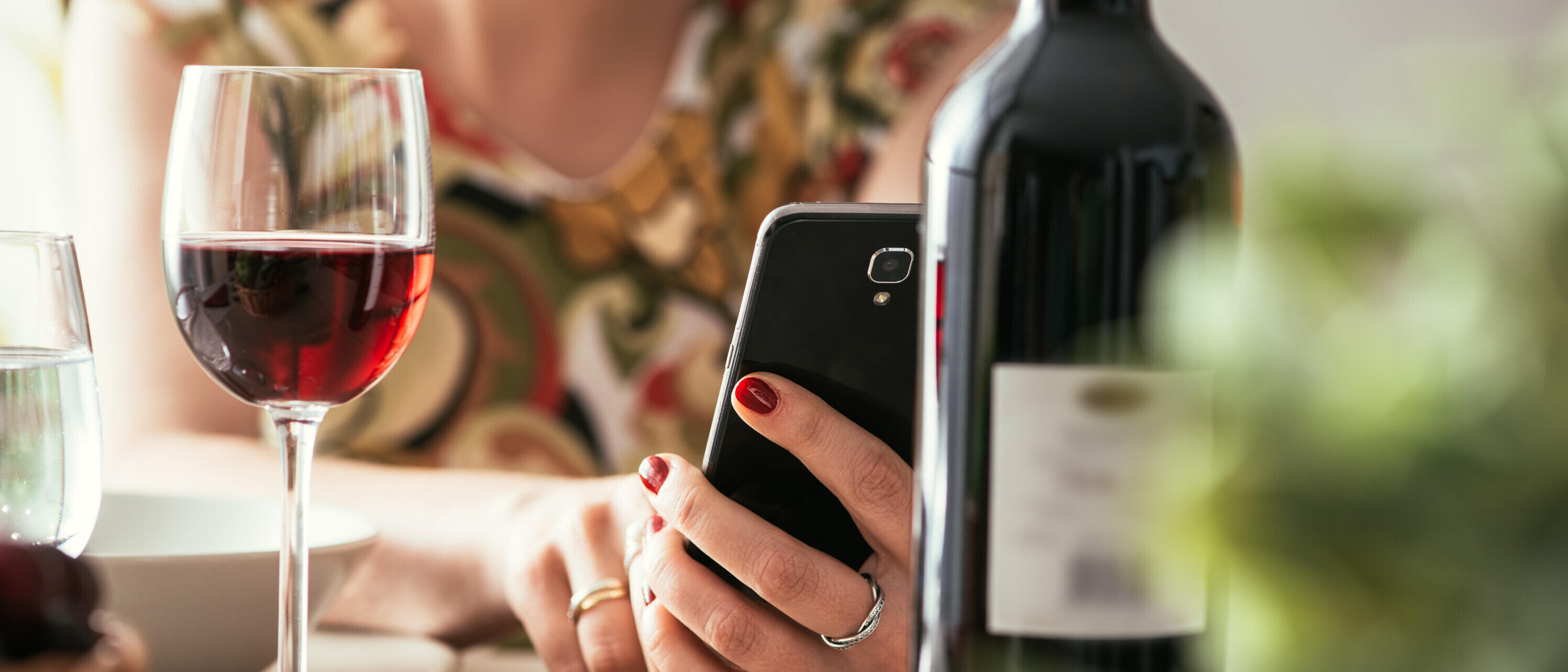 Woman using a wine app at the restaurant Symbolbild: Eine Frau hält ihr Smartphone in der Hand und trink ein Glas Wein.