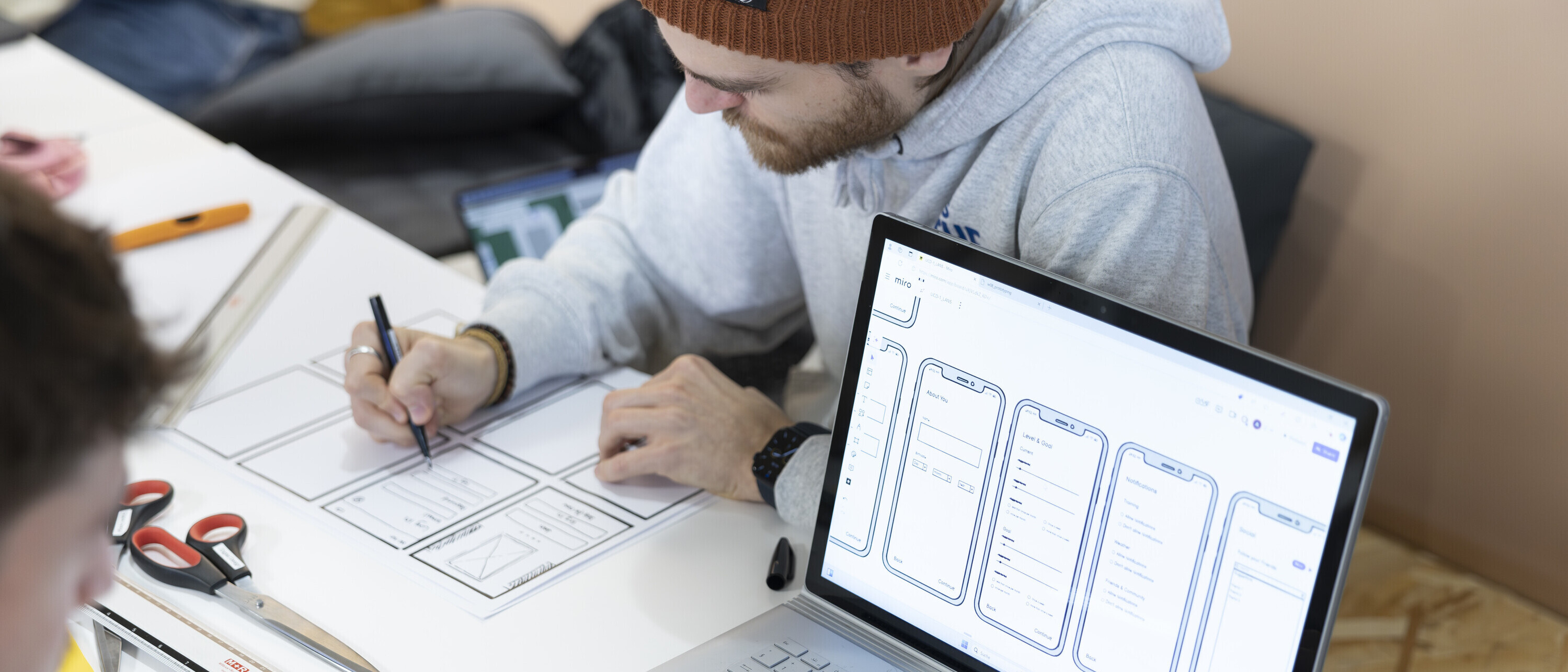 Bachelor Digital Design: Mann mit Laptop und Wireframe auf Display Ein Studierender des Bachelors Digital Design neben einem Laptop mit einem Wireframe